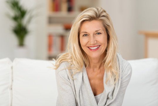 Blonde woman smiling on a white couch.
